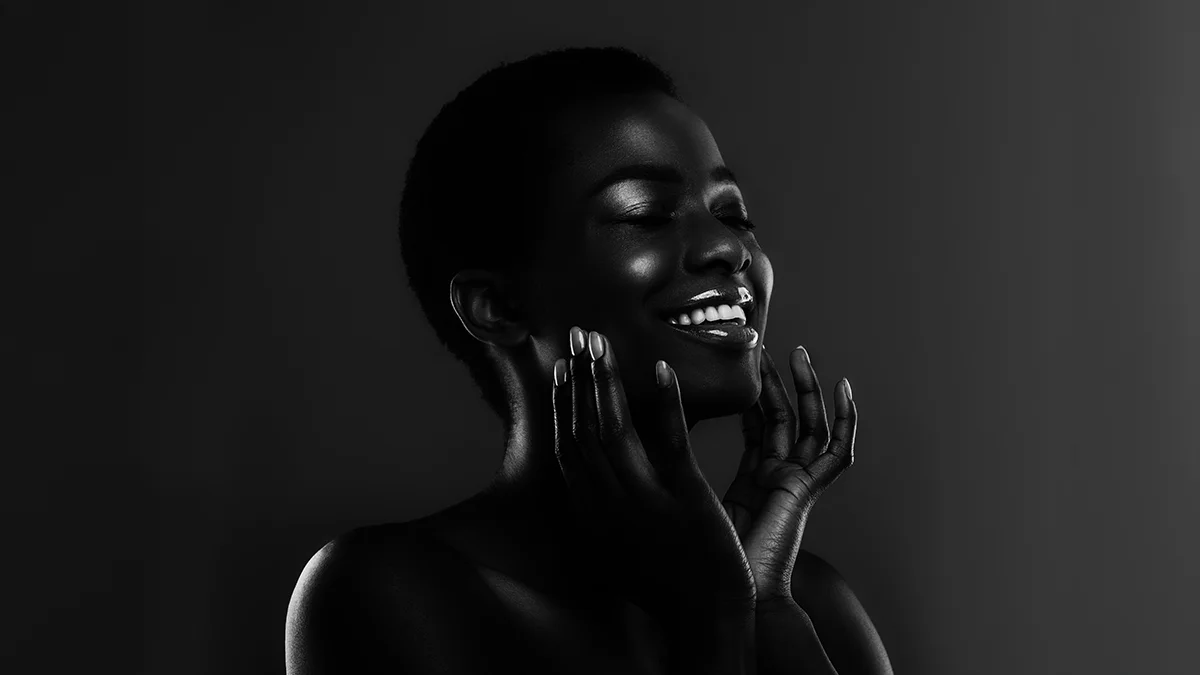 A very dark-skinned gorgeous african american woman with healthy glowing skn on a dark background